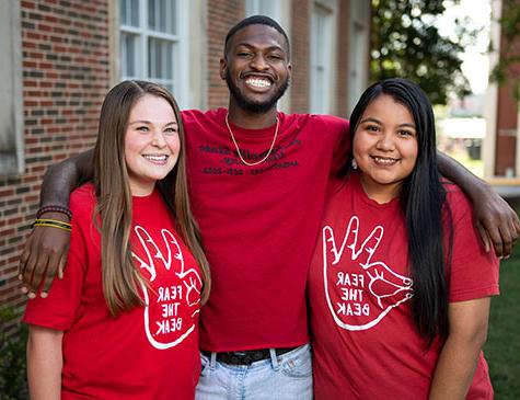 Three smiling JSU students wearing JSU tees embrace on the Quad